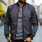 Homme portant un blouson bomber gris foncé, t-shirt gris, dans une rue urbaine floue. Mode masculine, style décontracté, tendance automne.