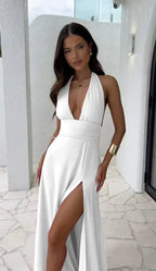 Femme en robe blanche élégante avec décolleté plongeant et fente haute, posant sur une terrasse moderne. Mode chic, style estival, tenue de soirée.