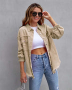 Jeune femme souriante portant une chemise beige décontractée, un top blanc et un jean bleu, posant avec des lunettes de soleil devant un mur gris.