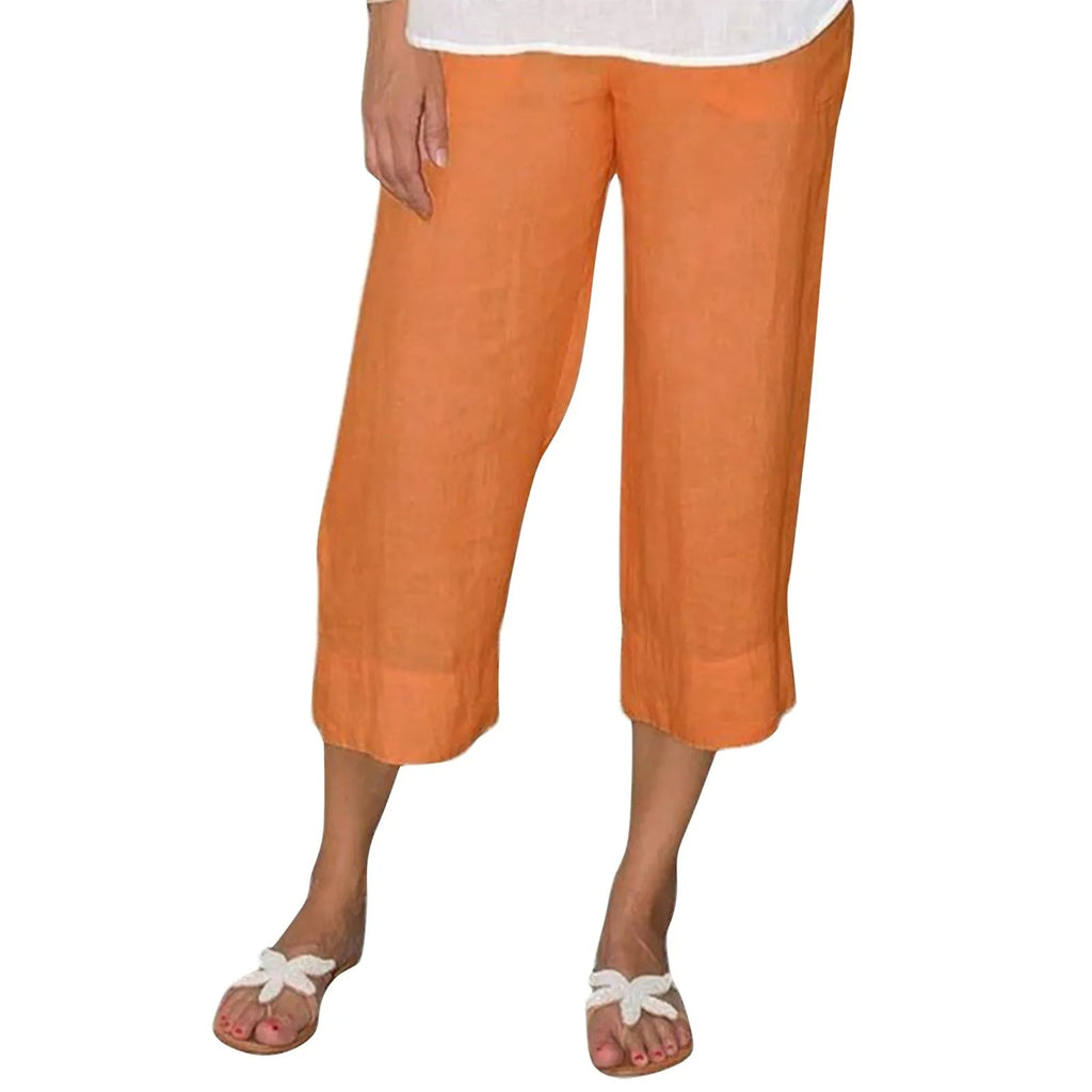Pantalon capri en lin orange pour femme, coupe ample, longueur mi-mollet, porté avec des sandales blanches à nœud. Mode estivale décontractée.