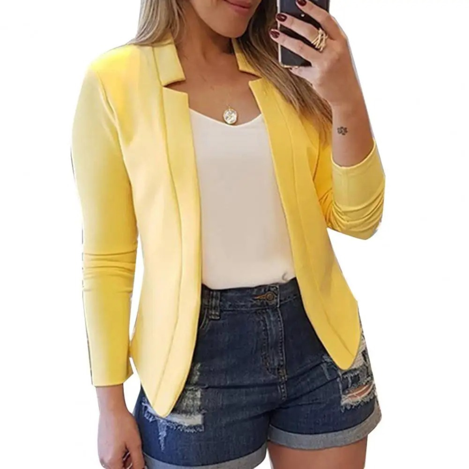 Femme portant un blazer jaune, débardeur blanc et short en jean déchiré, prenant un selfie. Mode décontractée, tendance printemps-été.