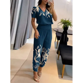 Femme portant une combinaison bleue à motifs floraux blancs, debout dans un salon moderne. Mode élégante, tenue décontractée chic, style estival.
