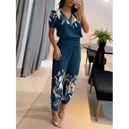 Femme portant une combinaison bleue à motifs floraux blancs, debout dans un salon moderne. Mode élégante, tenue décontractée chic, style estival.