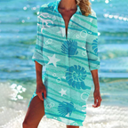 Robe de plage turquoise à motifs marins, étoiles de mer et coquillages, portée par une femme au bord de l'eau. Mode estivale, vacances plage.