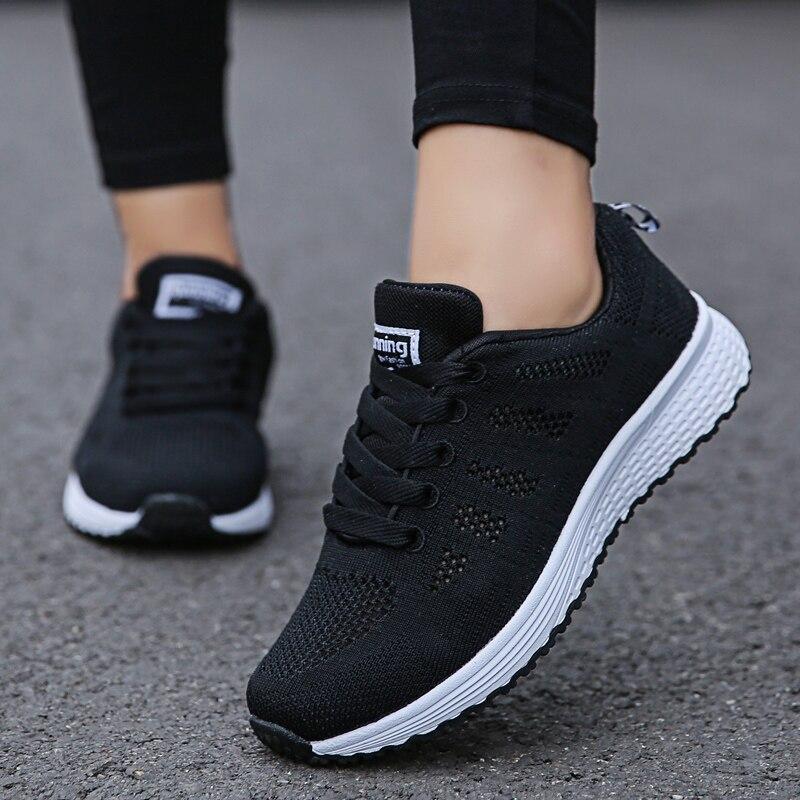 Chaussures de sport noires pour femme, semelle blanche, design respirant, idéales pour la course à pied et le fitness, portées sur un trottoir.