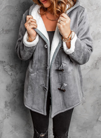 Femme portant un manteau en laine grise avec doublure en fourrure blanche, boutons en bois, sur fond de mur gris. Mode hiver élégante et confortable.