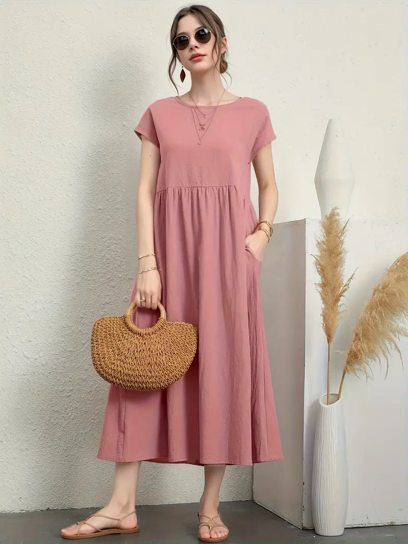 Femme en robe rose longue, portant un sac en osier, posant près de vases décoratifs. Mode estivale élégante, style décontracté chic.