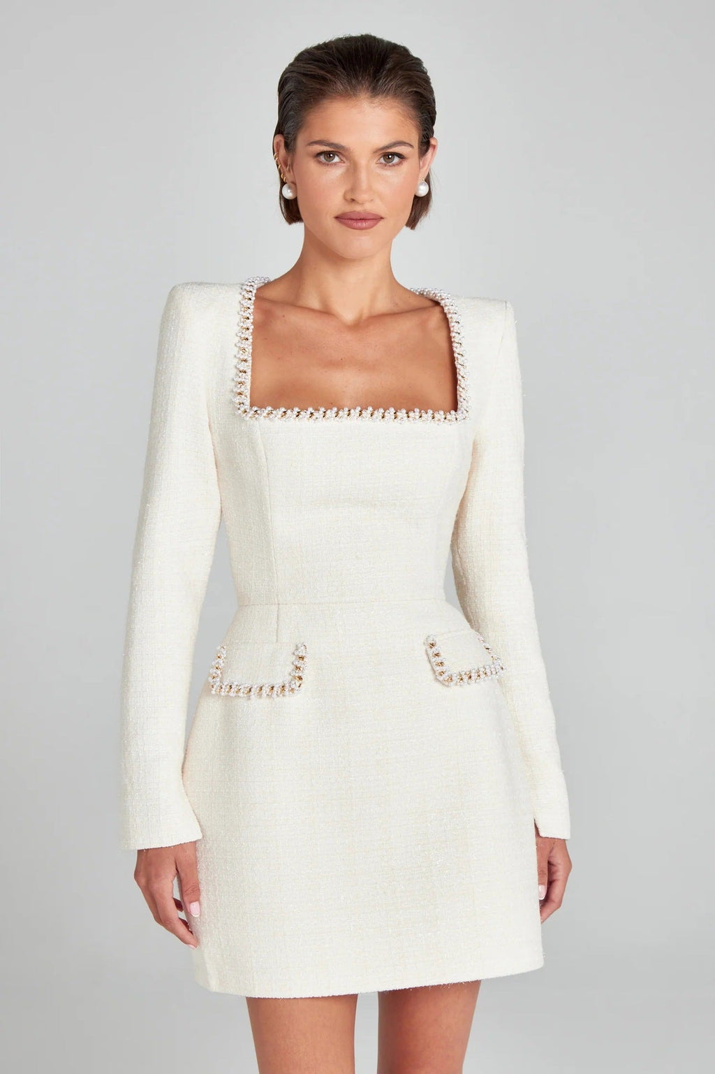 Robe blanche élégante à manches longues, col carré, ornée de détails perlés, portée par une femme. Mode féminine chic et sophistiquée.