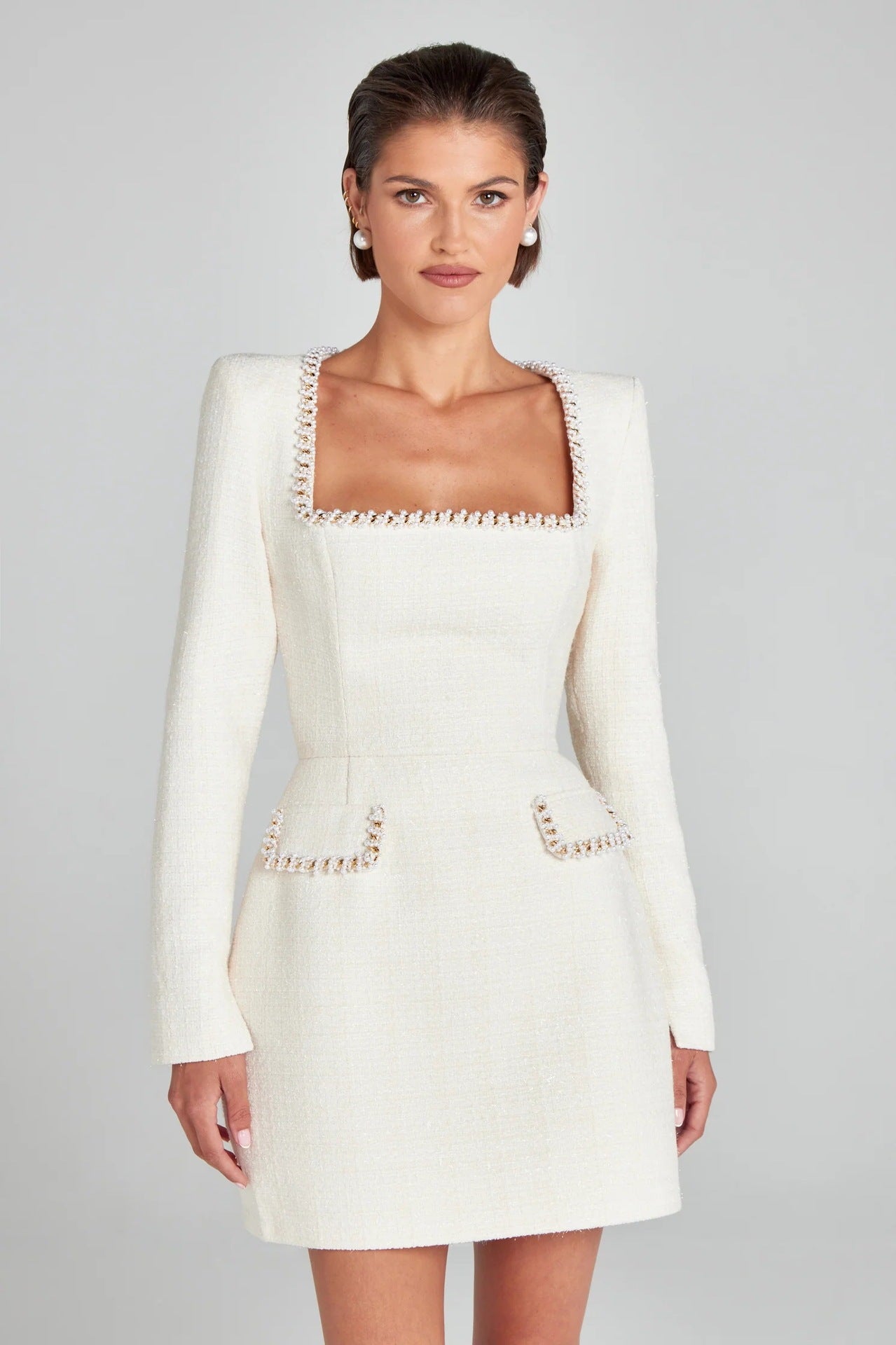 Robe blanche élégante à manches longues, col carré, ornée de détails perlés, portée par une femme. Mode féminine chic et sophistiquée.