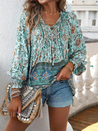 Femme en blouse bohème à motifs floraux verts et bleus, short en jean, tenant un sac à franges. Mode estivale, style décontracté chic.