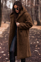 Femme portant un manteau en fausse fourrure marron, lunettes de soleil noires, dans un parc automnal. Mode hiver, style chic, promenade forêt.