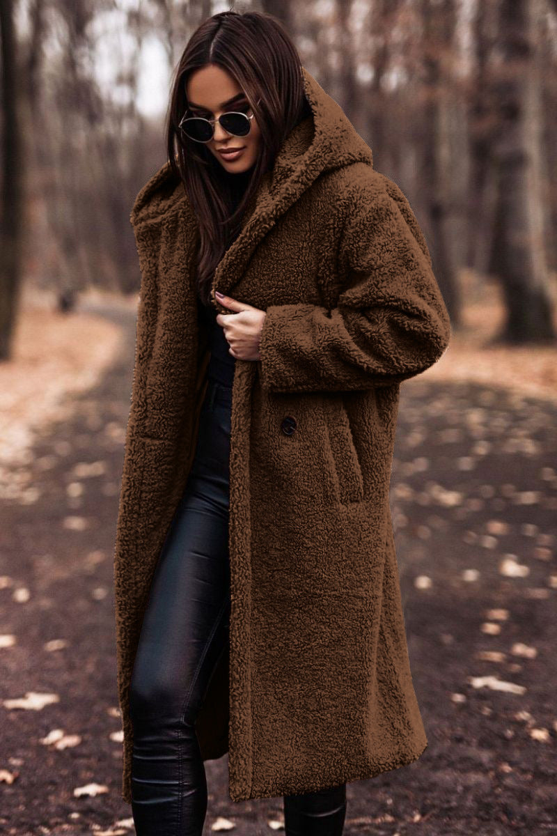 Femme portant un manteau en fausse fourrure marron, lunettes de soleil noires, dans un parc automnal. Mode hiver, style chic, promenade forêt.