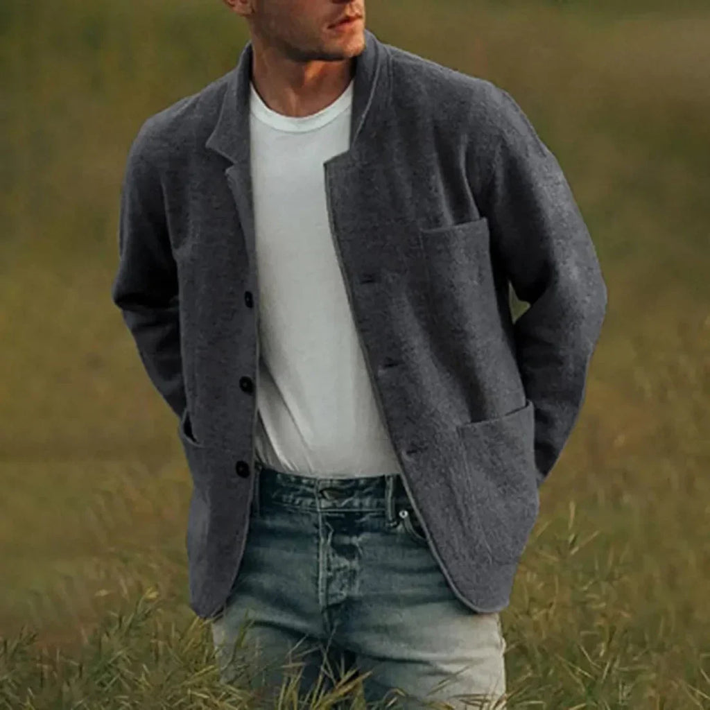 Homme portant une veste grise élégante sur un t-shirt blanc, debout dans un champ verdoyant. Mode masculine, style décontracté chic.