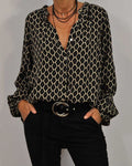 Chemisier à motifs géométriques noir et beige, manches longues, col ouvert, porté avec un pantalon noir et ceinture boucle ronde. Mode élégante femme.