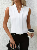 Femme en chemisier blanc élégant, tenant un café à emporter et une pochette noire, posant devant un mur texturé. Mode chic et moderne.
