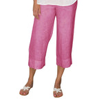 Pantalon capri rose en lin pour femme, coupe ample, longueur mi-mollet, porté avec des sandales blanches. Mode estivale décontractée.