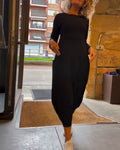 Femme en robe noire élégante, manches longues, sortant d'un bâtiment moderne. Mode urbaine, style chic, tenue décontractée.