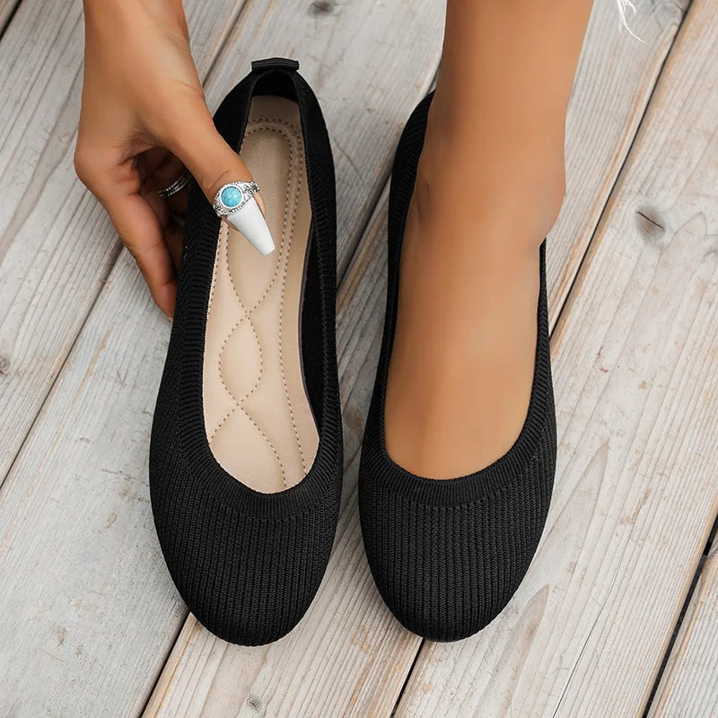 Ballerines noires élégantes sur plancher en bois, main ajustant une chaussure. Chaussures confortables pour femmes, style décontracté et moderne.