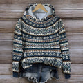 Pull-over en laine à motifs nordiques bleus et blancs, suspendu sur un cintre en bois, avec un short en jean, sur fond de bois rustique.