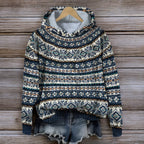 Pull-over en laine à motifs nordiques bleus et blancs, suspendu sur un cintre en bois, avec un short en jean, sur fond de bois rustique.