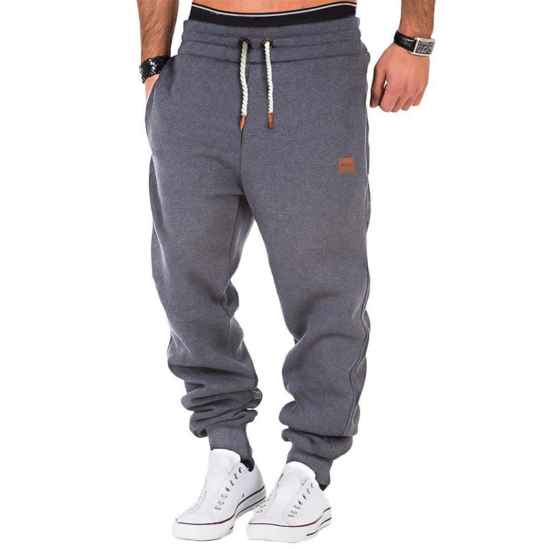 Homme portant un pantalon de jogging gris, cordons blancs, baskets blanches. Mode décontractée, tenue sportive, style urbain.