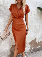Robe midi orange élégante, manches courtes, col en V croisé, fente latérale, portée par une femme blonde tenant une pochette beige.
