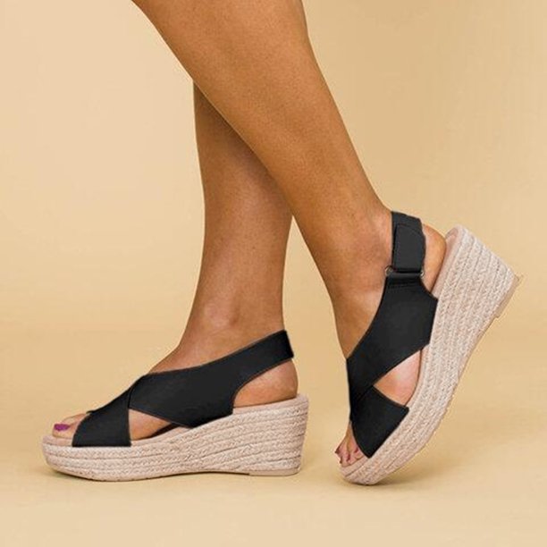 Sandales compensées noires pour femme avec semelle en corde, design croisé, portées sur fond beige. Chaussures d'été élégantes et confortables.