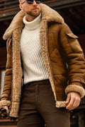 Homme portant un manteau aviateur en peau de mouton marron avec col en fourrure, pull blanc à col roulé, lunettes de soleil, style hiver élégant.