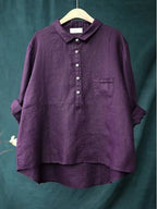Chemise en lin violet foncé pour femme, manches longues retroussées, col boutonné, poche poitrine, suspendue sur un cintre en bois.