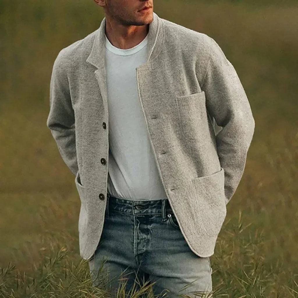 Homme portant un cardigan gris en laine, t-shirt blanc et jeans, debout dans un champ. Mode masculine décontractée, style automnal élégant.