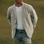 Homme portant un cardigan gris en laine, t-shirt blanc et jeans, debout dans un champ. Mode masculine décontractée, style automnal élégant.