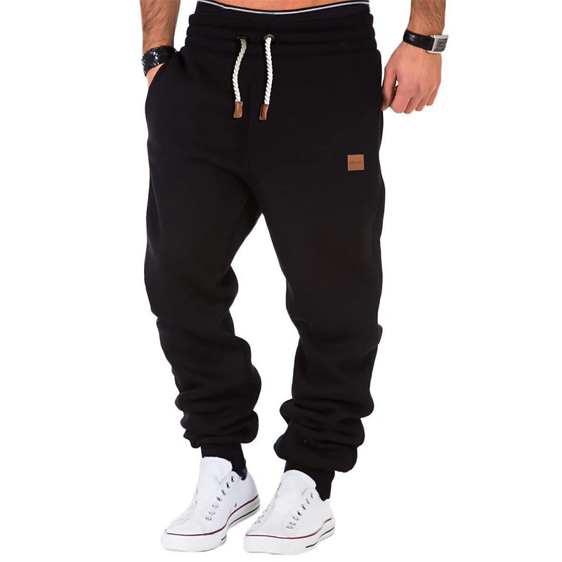 Pantalon de jogging noir pour homme avec cordon de serrage blanc, poches latérales, porté avec des baskets blanches. Mode décontractée masculine.