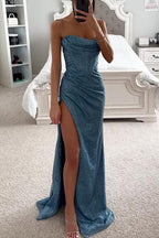 Robe de soirée bleue scintillante avec fente haute, portée par une femme dans une chambre élégante. Mode glamour, tenue de soirée chic.