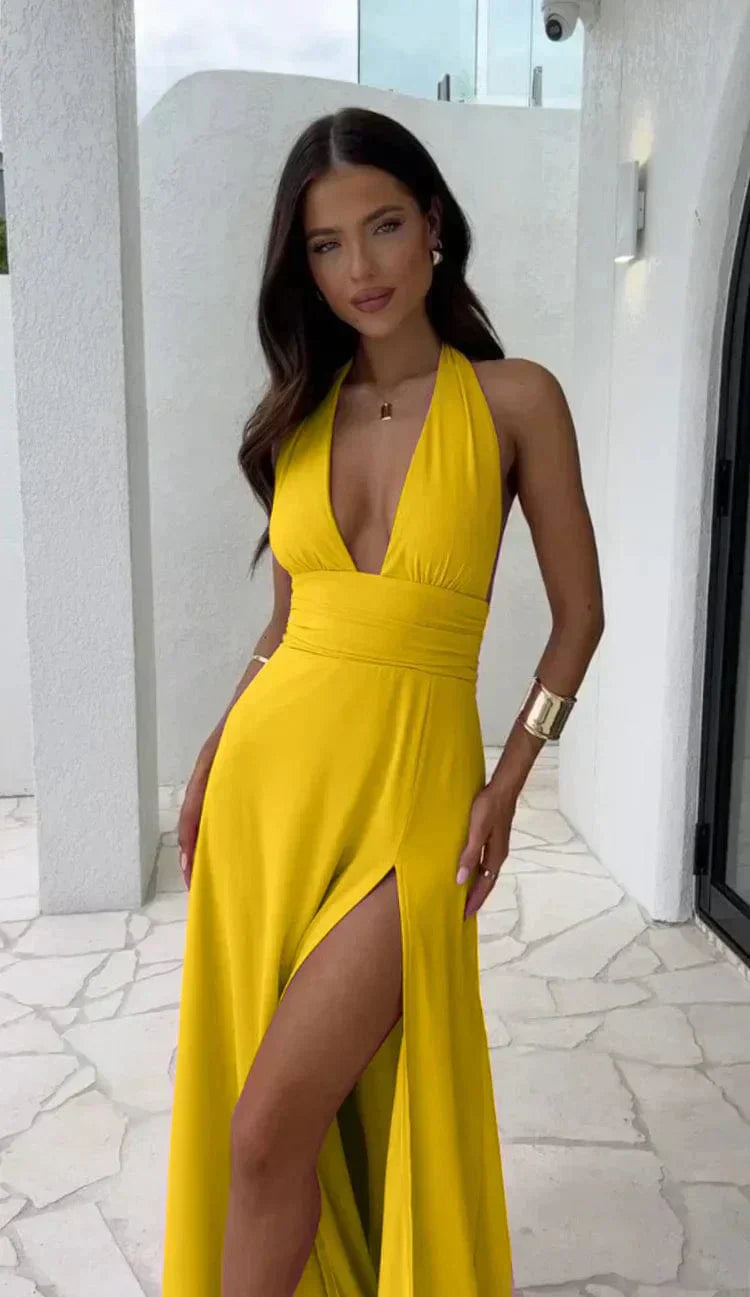 Femme en robe jaune élégante avec décolleté plongeant et fente haute, posant sur une terrasse moderne. Mode estivale, style chic et glamour.