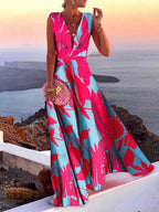 Robe longue femme, motif floral rose et bleu, col en V, sans manches, tenue élégante pour soirée d'été, vue sur mer au coucher du soleil.