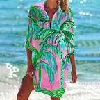 Robe de plage rose à motifs de palmiers verts, femme au bord de la mer, tenue estivale colorée, mode plage, vacances tropicales.