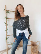 Femme portant un pull tricoté gris, posant devant une échelle en bois décorée de plantes. Mode automne-hiver, style décontracté, intérieur moderne.