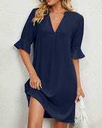 Robe bleu marine élégante avec manches mi-longues et col en V, portée par une femme blonde. Mode féminine chic, tenue décontractée.