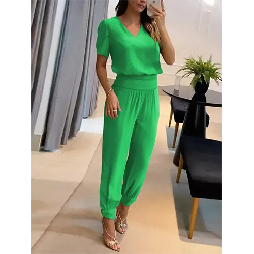 Femme en ensemble vert élégant, blouse à manches courtes et pantalon ample, posant dans un salon moderne. Mode féminine chic et tendance.