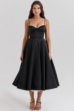 Robe noire élégante mi-longue avec bretelles fines, jupe évasée, portée par une femme. Mode féminine chic, tenue de soirée sophistiquée.