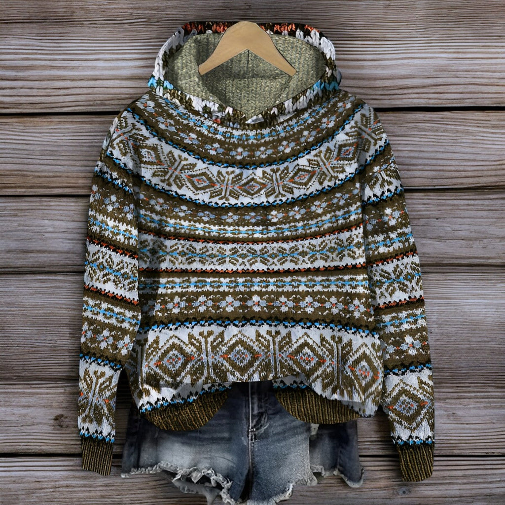 Pull-over en laine à motifs nordiques suspendu sur un cintre en bois, accompagné d'un short en jean déchiré, sur fond de planches en bois.