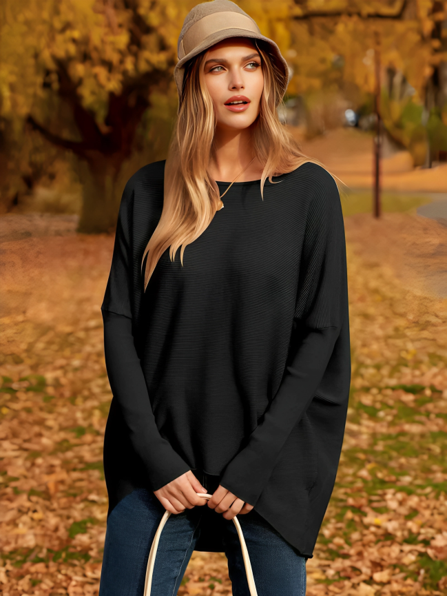Femme en pull noir et chapeau beige, debout dans un parc automnal avec feuilles dorées. Mode automne, style décontracté, nature.