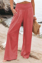 Pantalon large rose en lin pour femme, style décontracté, bord de mer. Mode estivale, tenue confortable, accessoire sac en paille.
