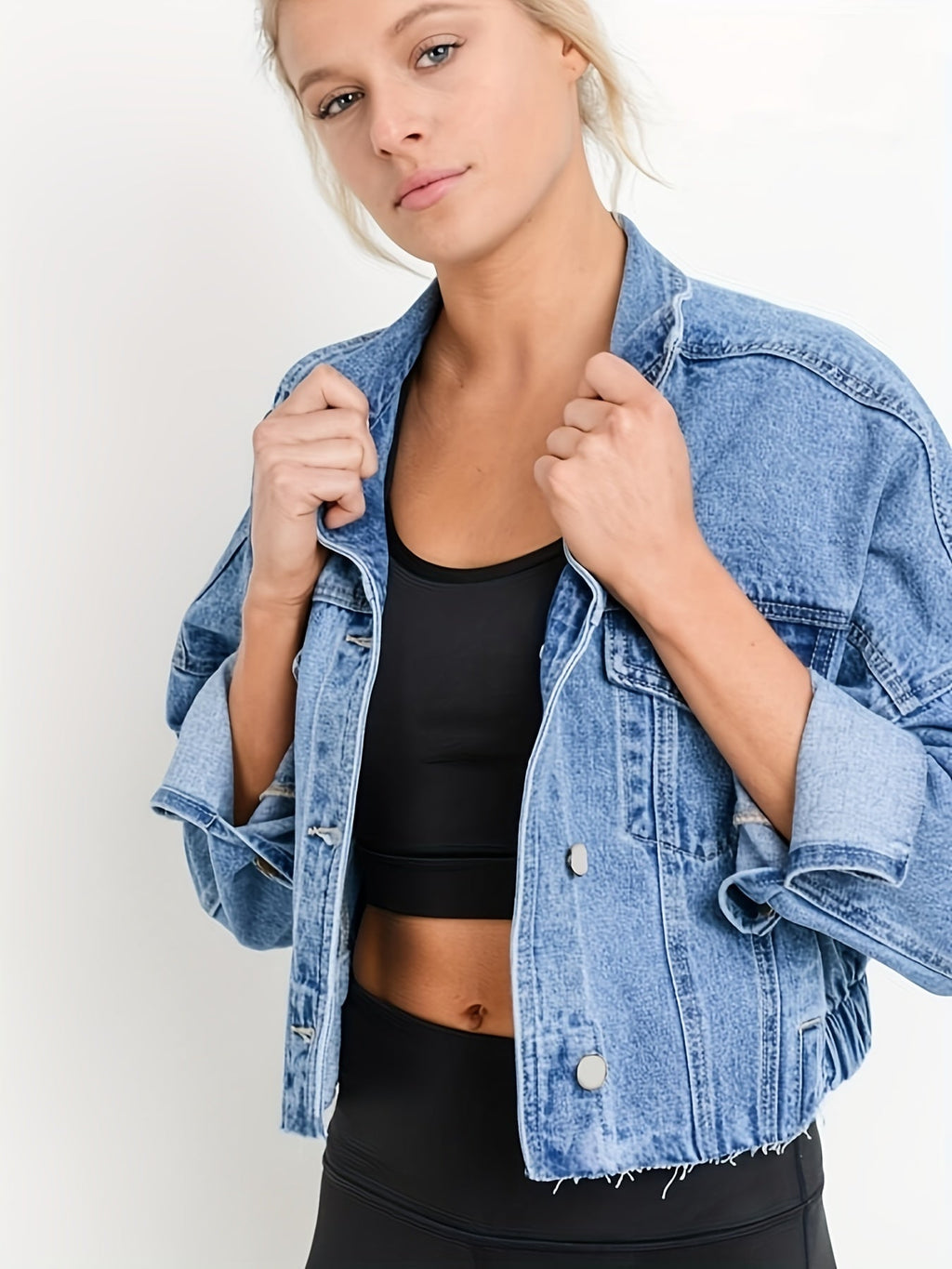 Jeune femme portant une veste en jean bleu sur un débardeur noir, posant contre un fond blanc. Mode décontractée, style moderne, tendance vestimentaire.