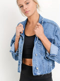 Jeune femme portant une veste en jean bleu sur un débardeur noir, posant contre un fond blanc. Mode décontractée, style moderne, tendance vestimentaire.