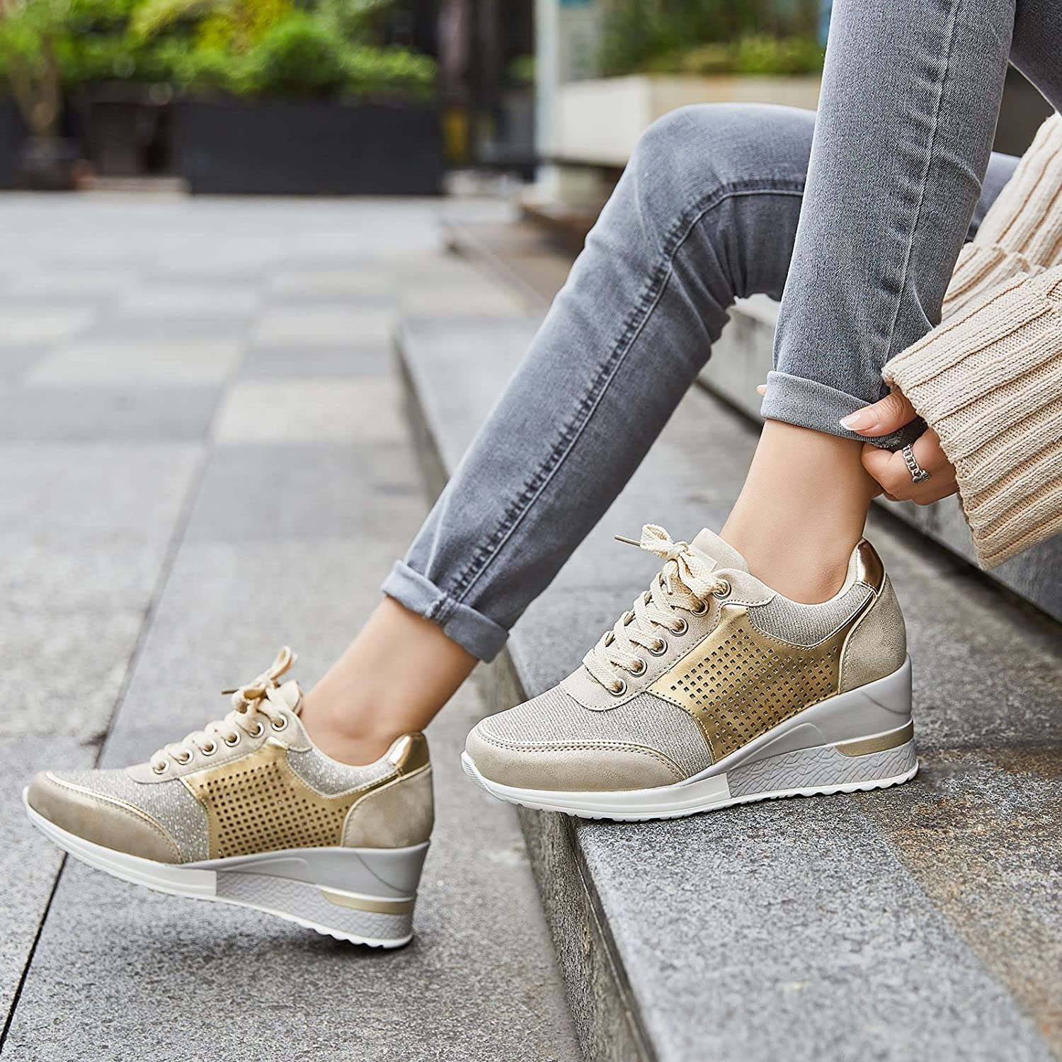 Femme portant des baskets compensées dorées, assise sur des marches en extérieur. Chaussures mode tendance, confortables et élégantes pour la marche.