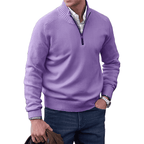 Homme portant un pull violet à col zippé, chemise blanche, jean bleu, montre argentée, tenant une veste marron. Mode masculine élégante et décontractée.