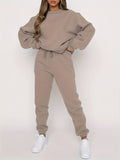 Femme portant un ensemble de survêtement beige, composé d'un sweat ample et d'un pantalon de jogging, avec des baskets blanches. Mode décontractée.