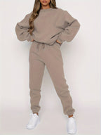 Femme portant un ensemble de survêtement beige, composé d'un sweat ample et d'un pantalon de jogging, avec des baskets blanches. Mode décontractée.