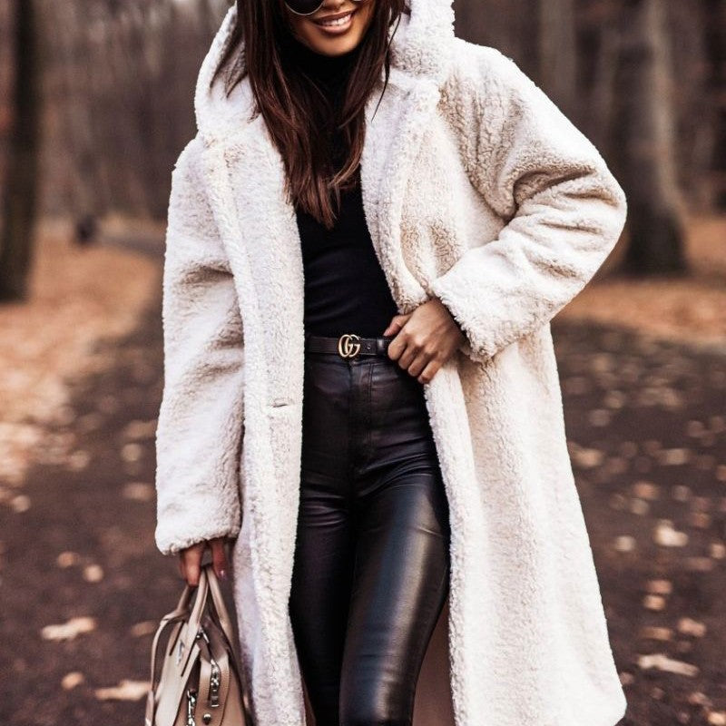 Femme portant un manteau en fausse fourrure blanche, pantalon en cuir noir, lunettes de soleil, tenant un sac à main beige, dans un parc automnal.